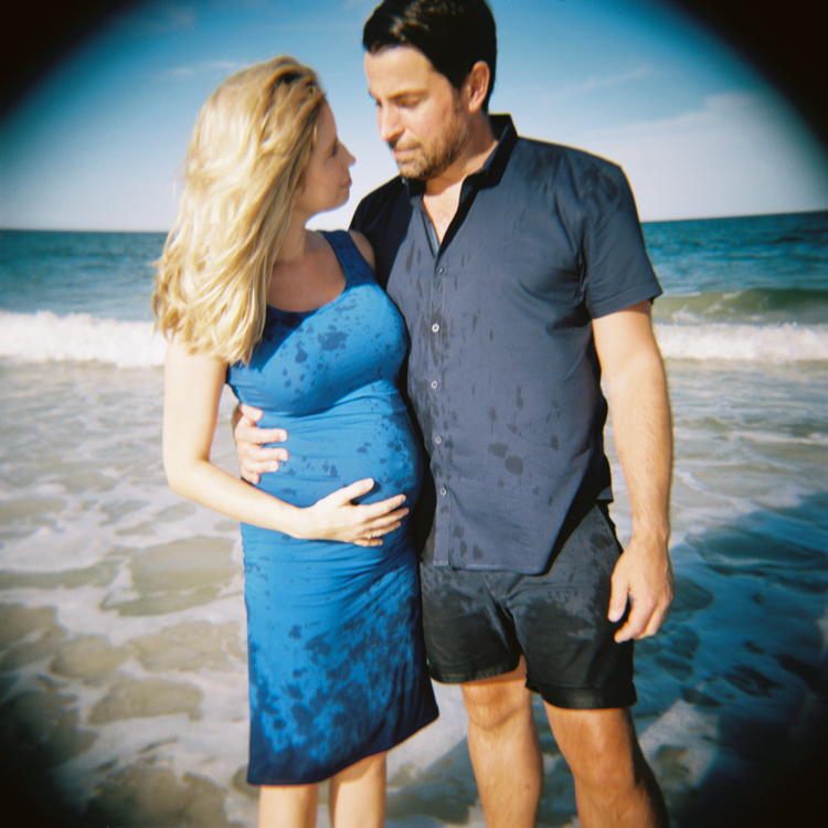 pregnant woman and husband looking at each other standing in the ocean