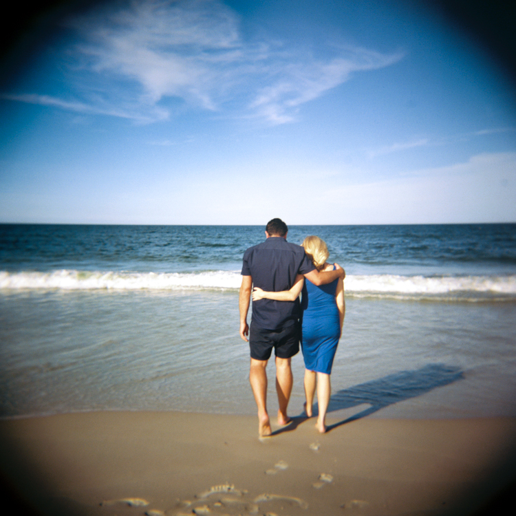 couple with their arms around each others shoulders walking toward the ocean
