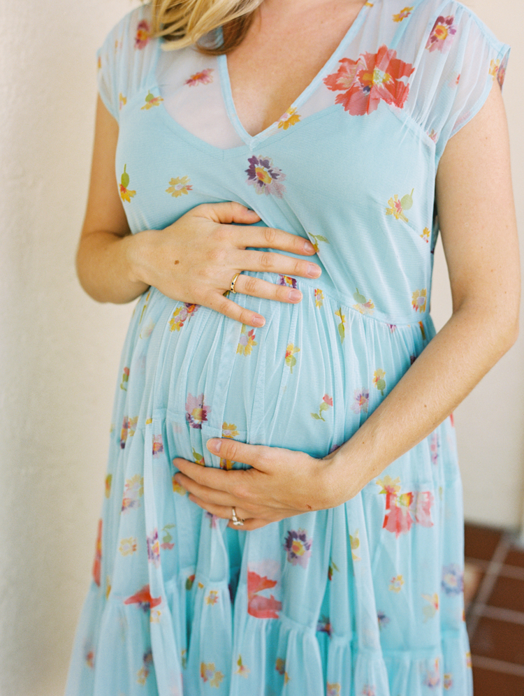 pregnant woman in blue dress with flowers putting her hands on her belly