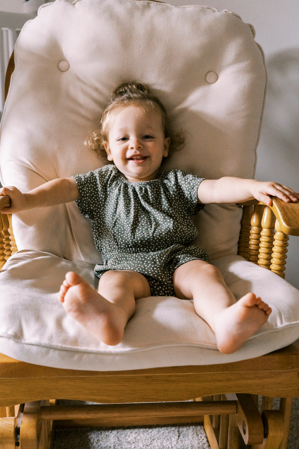 toddler girl in green romper sitting in large rocking chair smiling