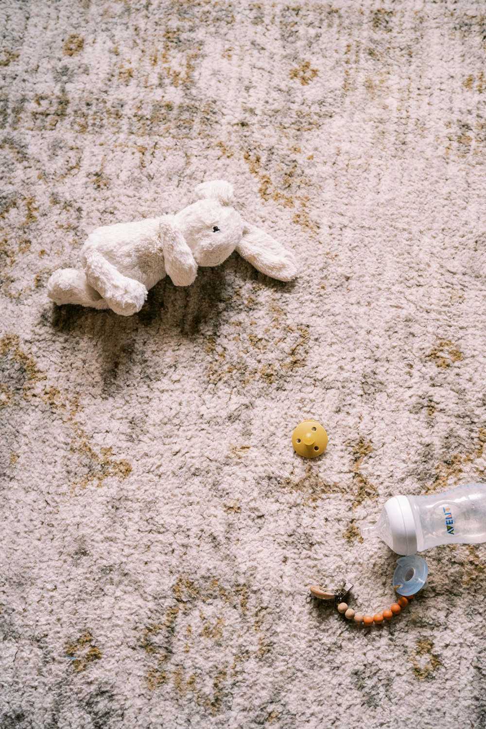 white stuffed bunny toy and baby bottle lying on tan traditional carpet