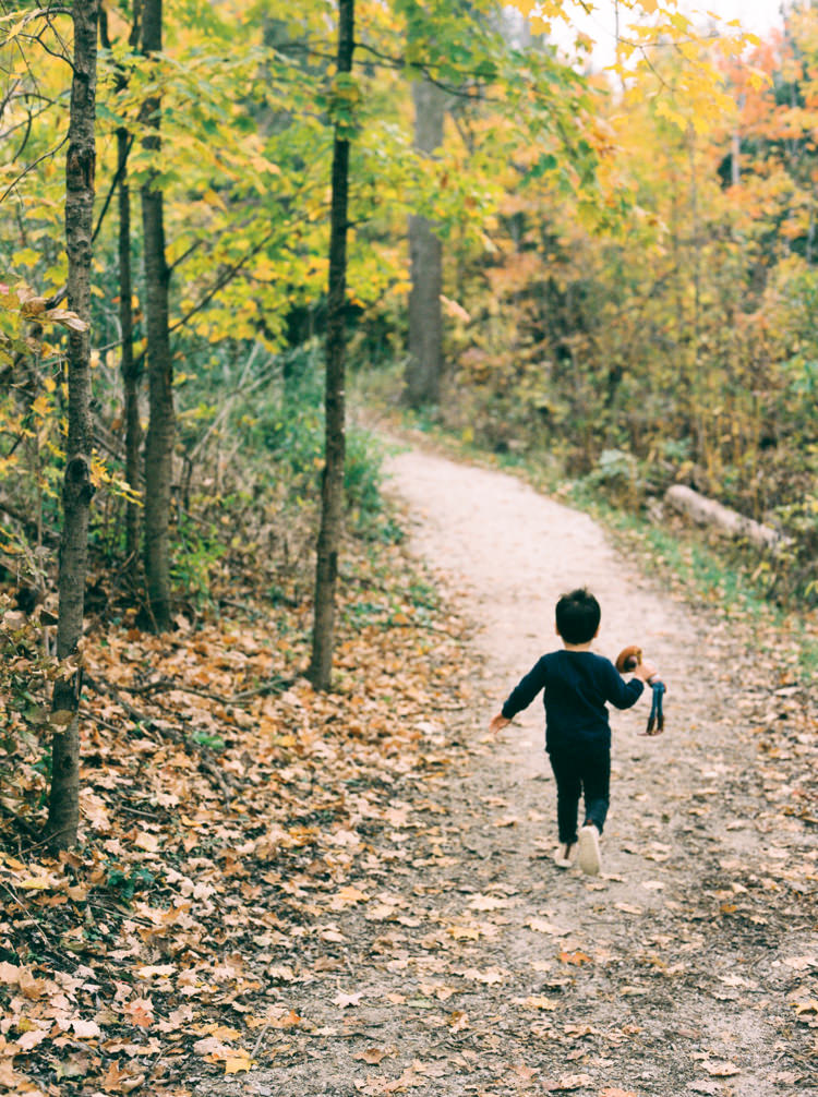 toddler holding toy and running down path in an autumn forest