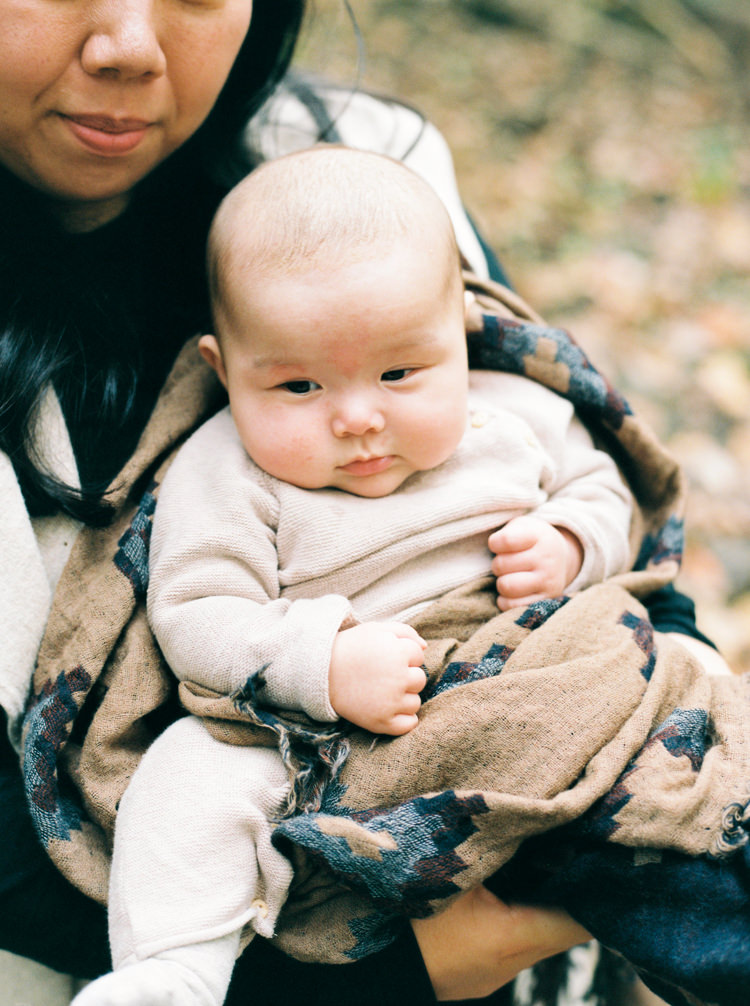 mom holding baby in tan romper wrapped in brown blanket