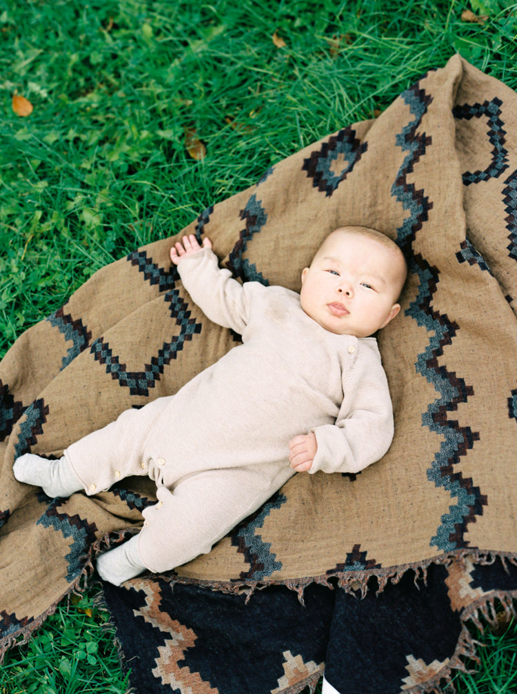 baby in tan jumpsuit lying on the grass on a brown blanket