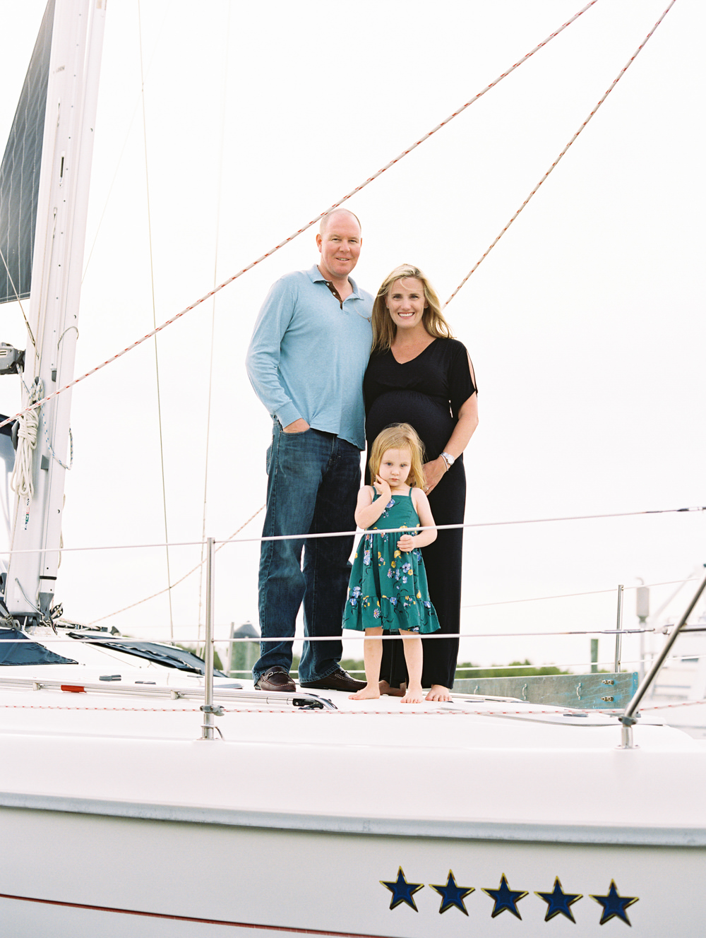 family of three standing together on sailboat smiling at the camera