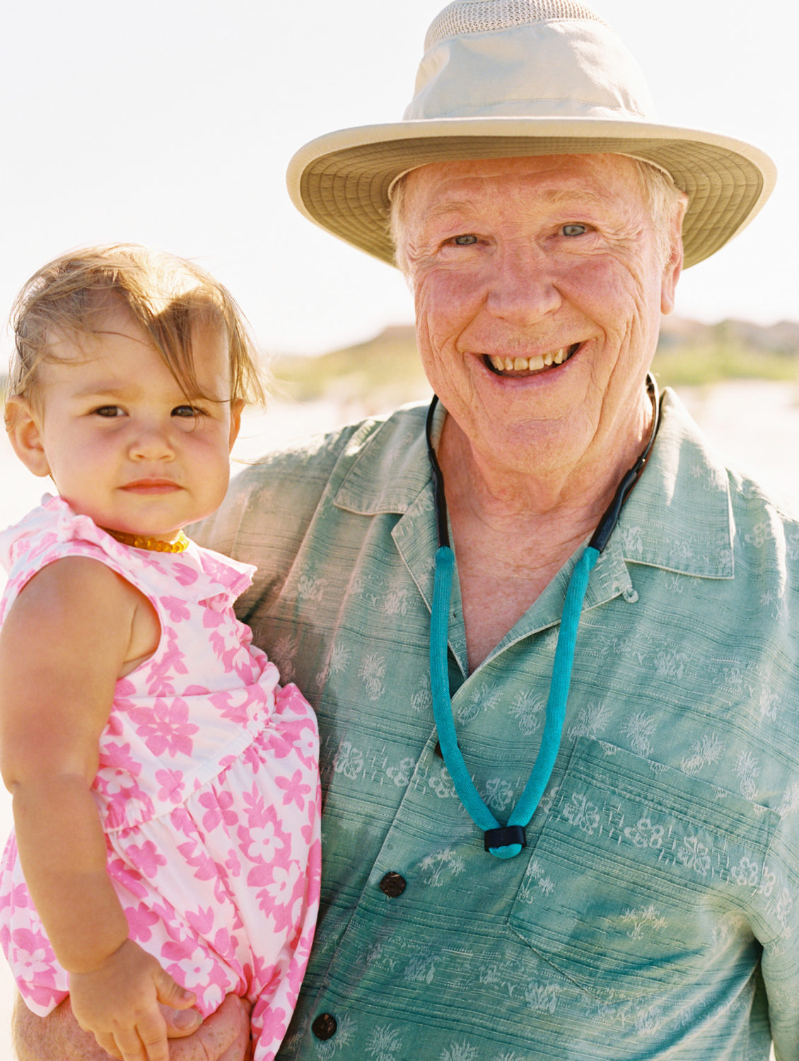 a grandpa in green shirt and hat holding baby grandaughter and smiling