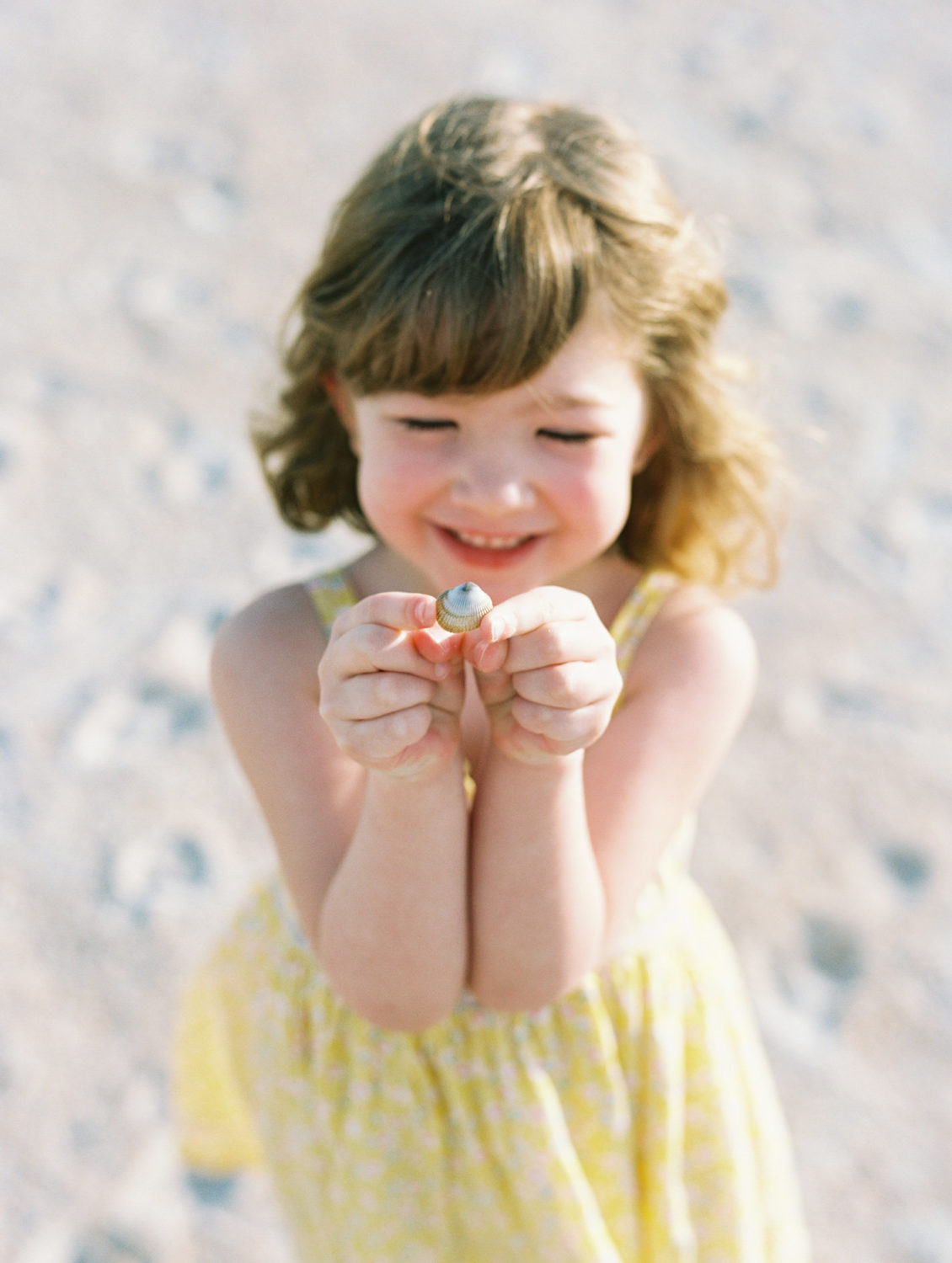 little girl in yellow dress holding tiny seashell and smiling