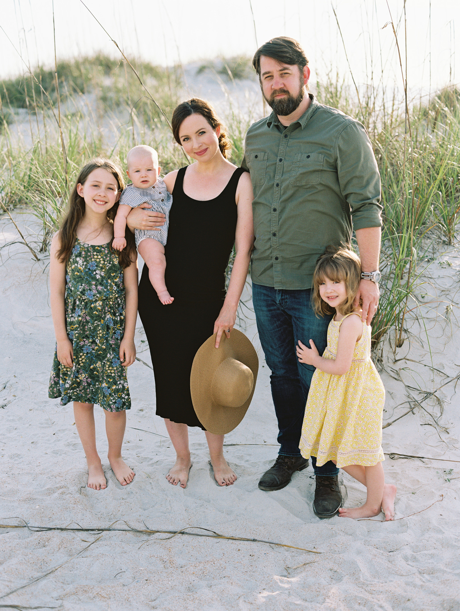 Family of five standing close together and looking at camera on dunes at the beach