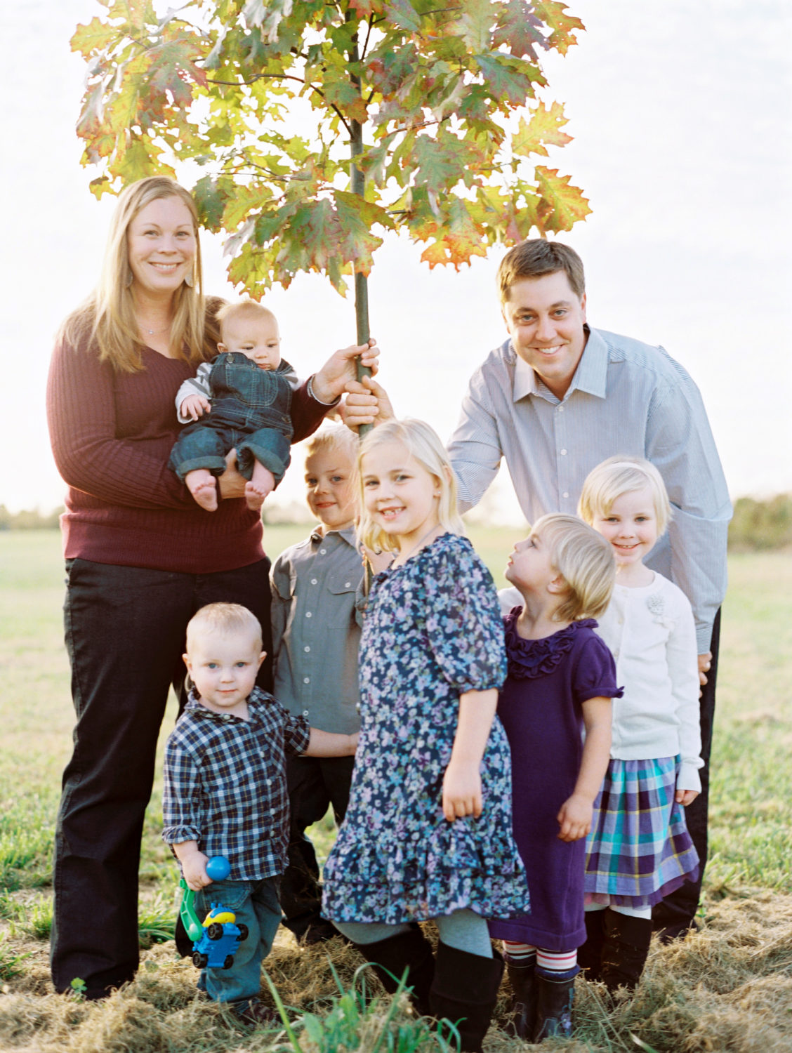 Family of eight standing around a young tree in their yard and smiling