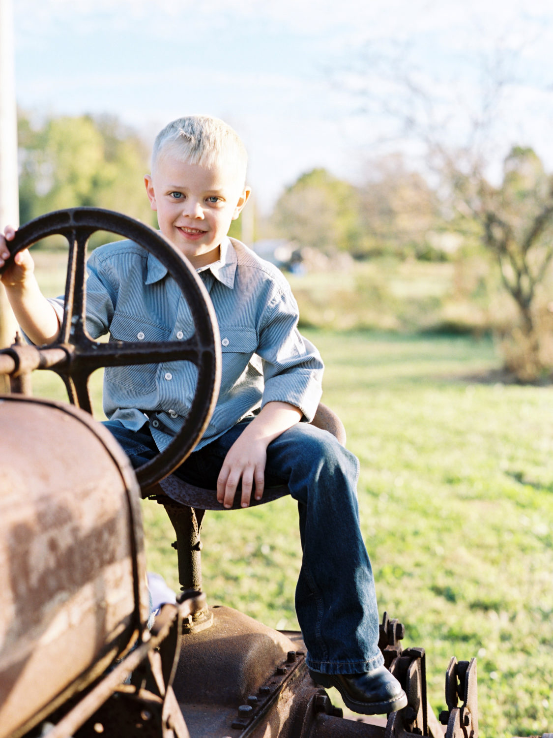young blonde boy sitting on a rusty antique tractor and smiling