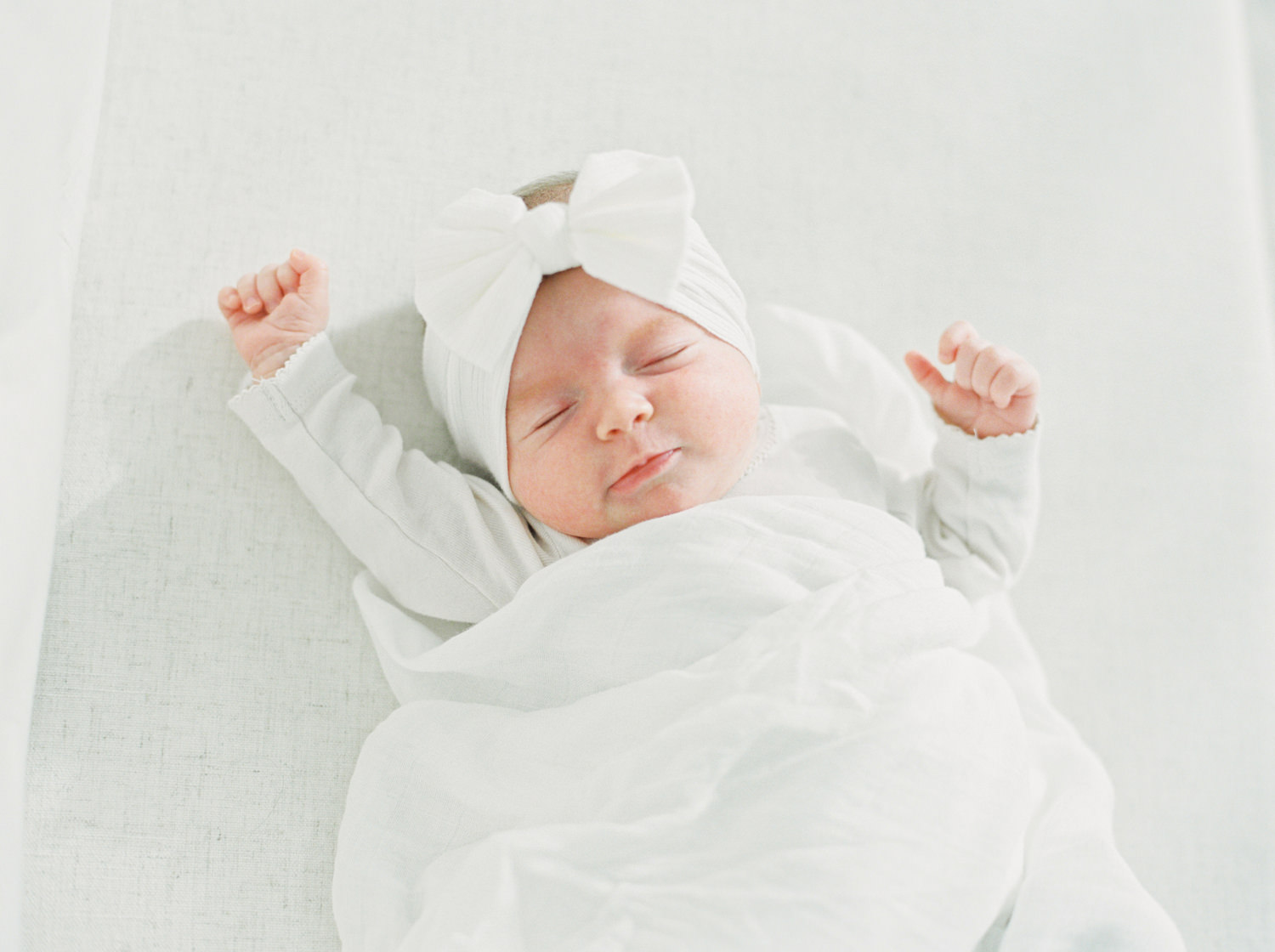 sleeping baby in white clothes and white blanket sleeping on a cream color couch and stretching