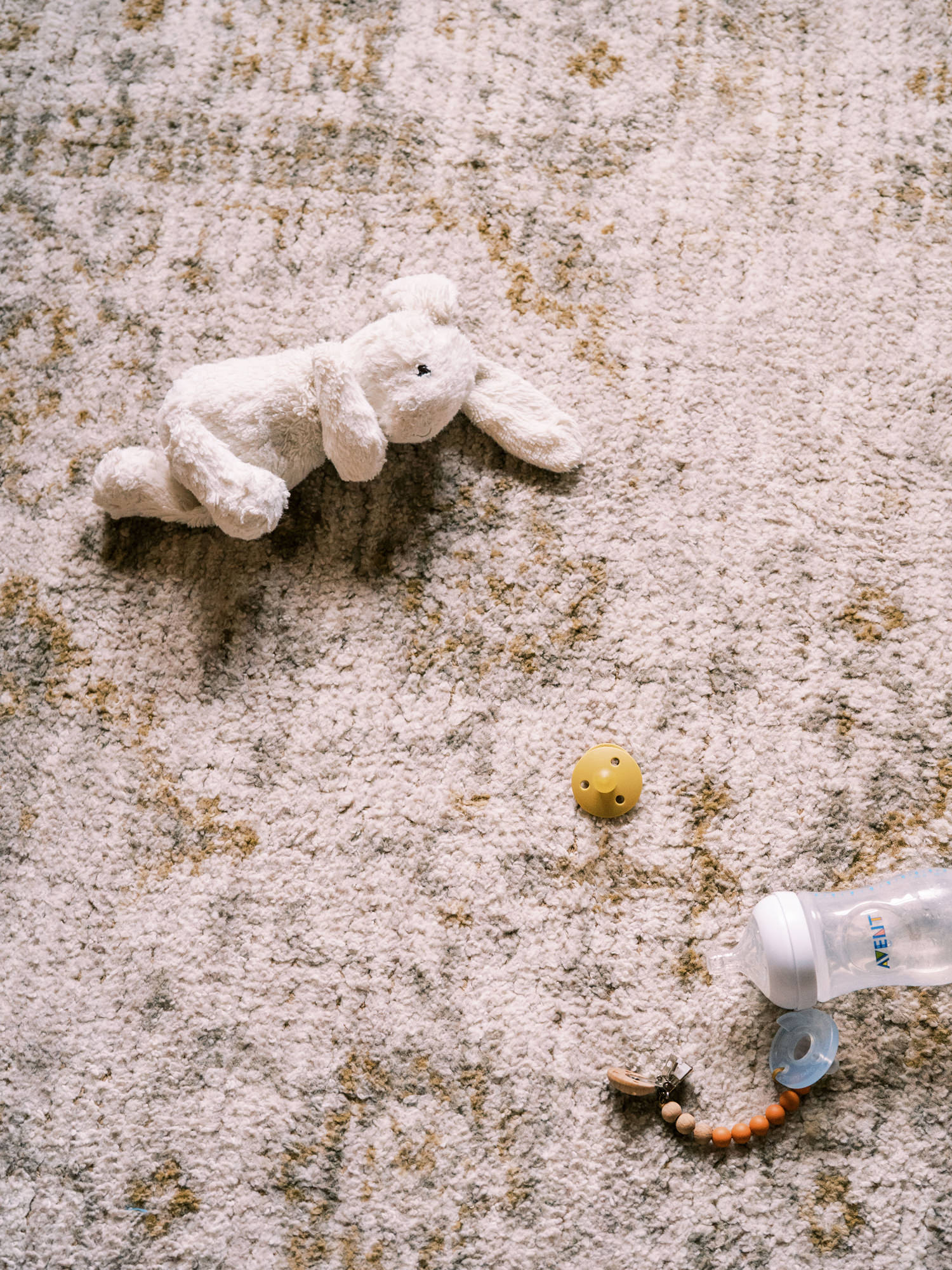 child's plush white rabbit toy lying on a tan Persian rug with a bottle and pacifier tossed nearby