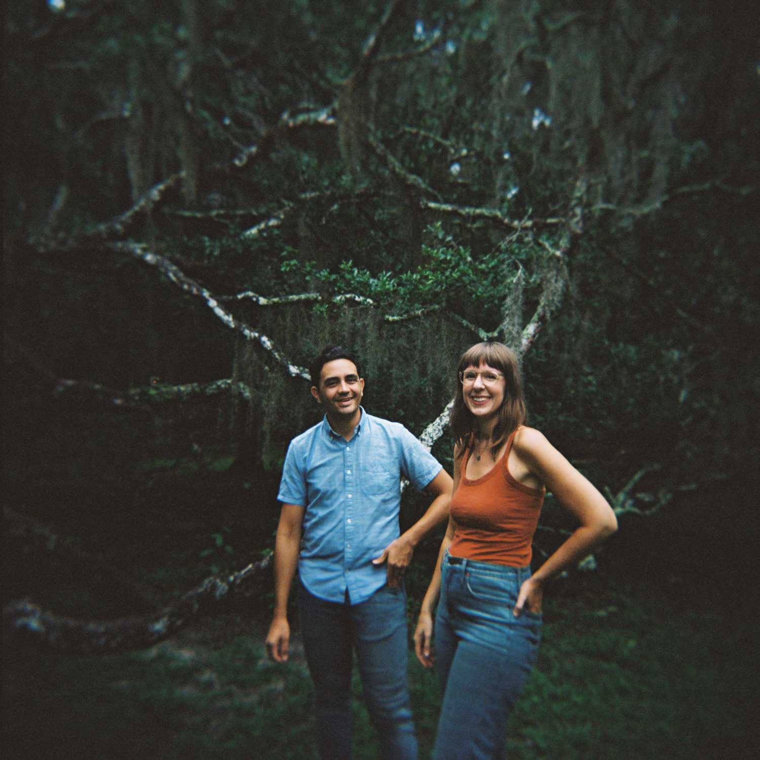 husband and wife standing next to each other in front of a tangle of oak tree branches and moss