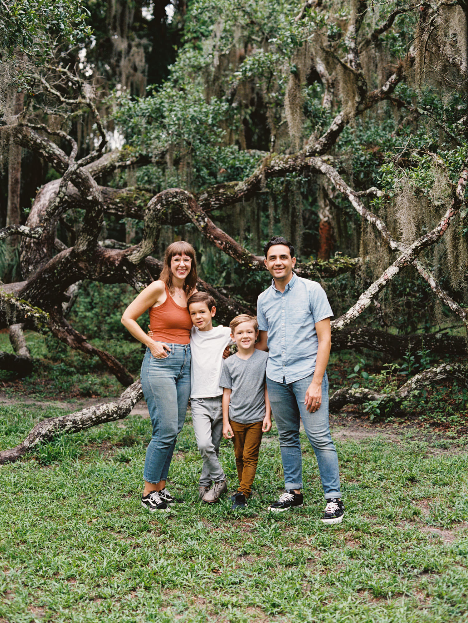 two brothers standing in between mom and dad with their arms around them smiling in a Florida summer forest