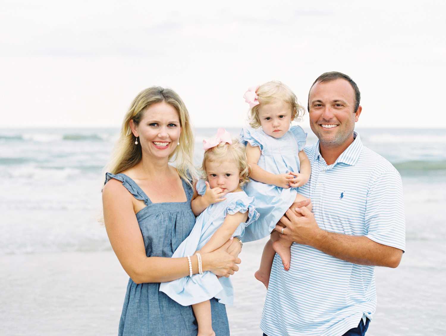 Man, woman and their twin girls dressed in blue standing in front of the ocean and smiling