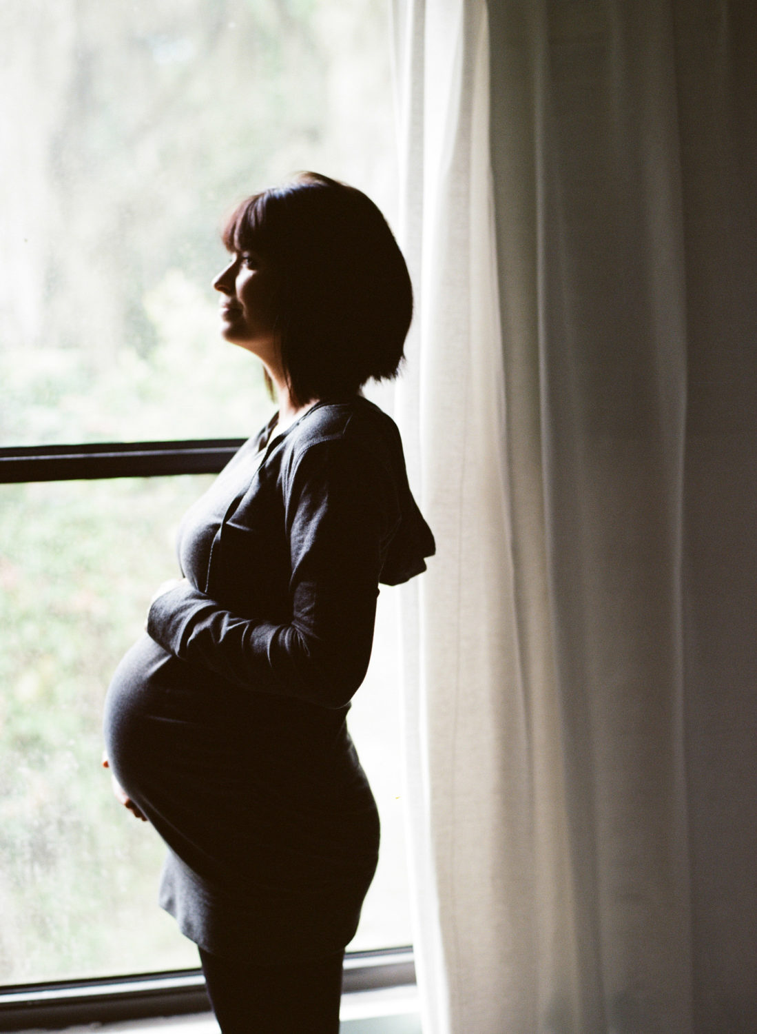 silhouette of pregnant woman with short hair standing in front of a window 