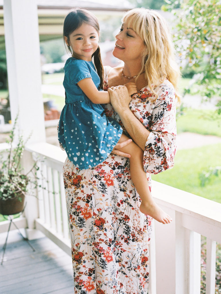 pregnant mother with long blonde hair and floral dress holding her toddler and smiling at her