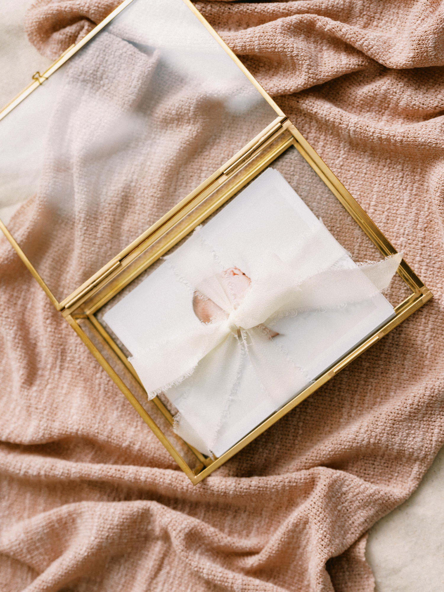 glass and brass box with prints of newborn photos tied with a pink ribbon