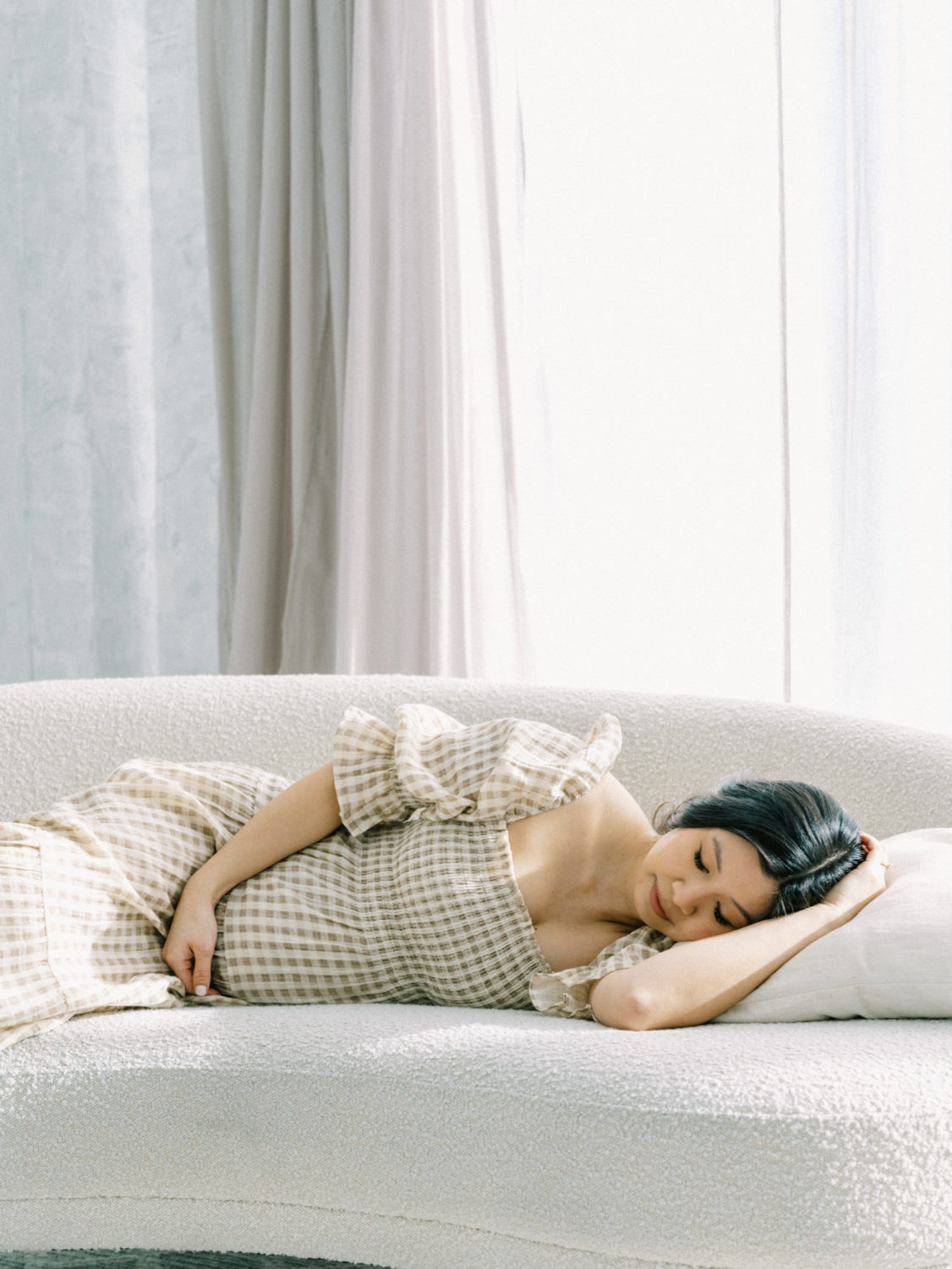 pregnant asian woman lying on her side on a minimalist couch resting her head on her hand with her eyes closed