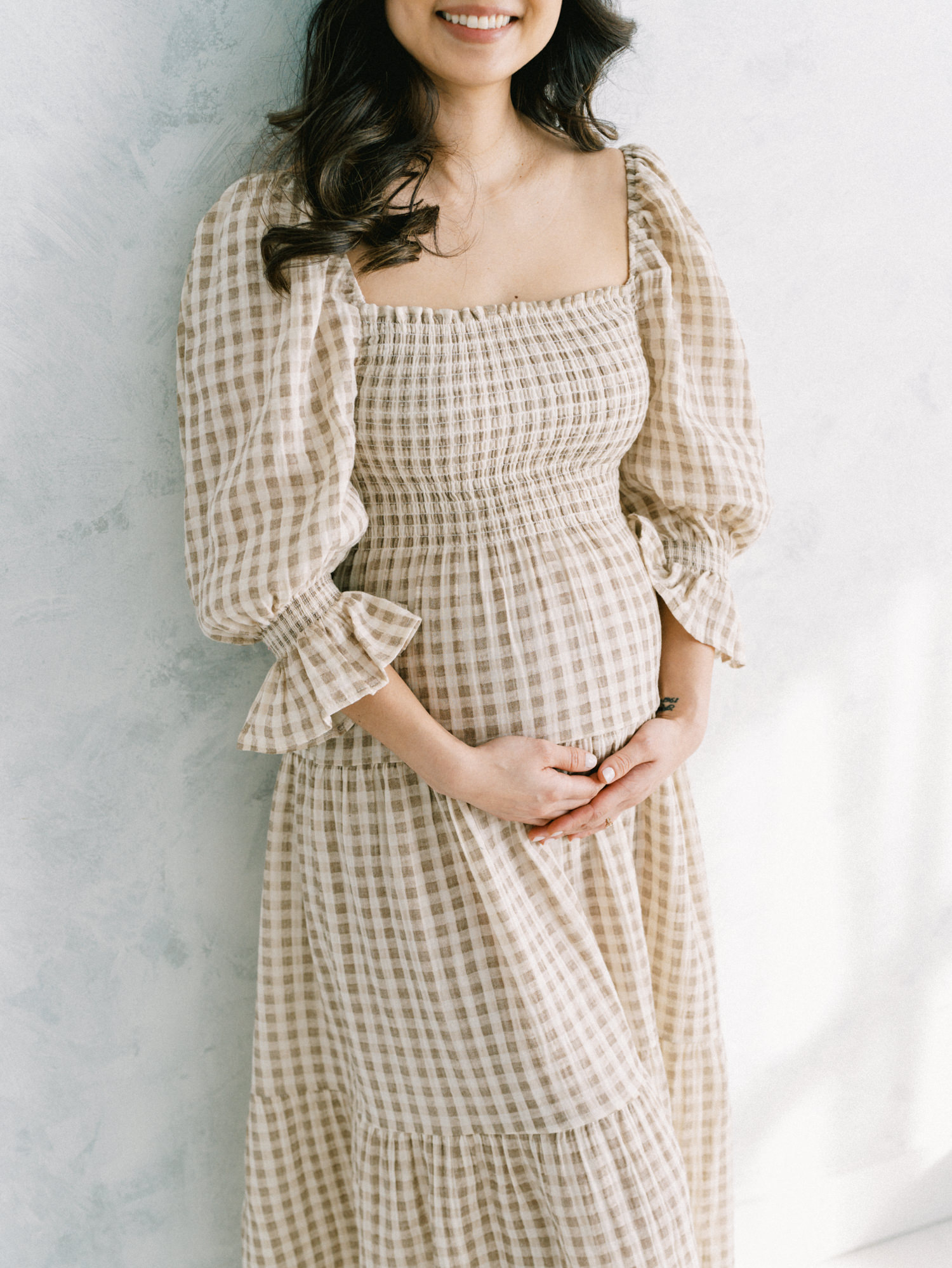 cropped image showing just the smile and torso of an expecting mother cradling her belly and wearing a beautiful simple maternity dress