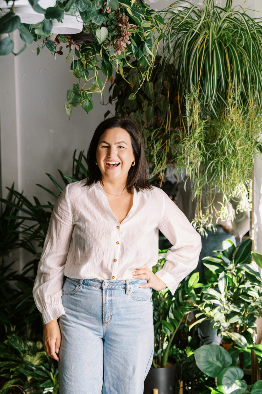 working mom in white blouse and jeans smiling surrounded by lush plants