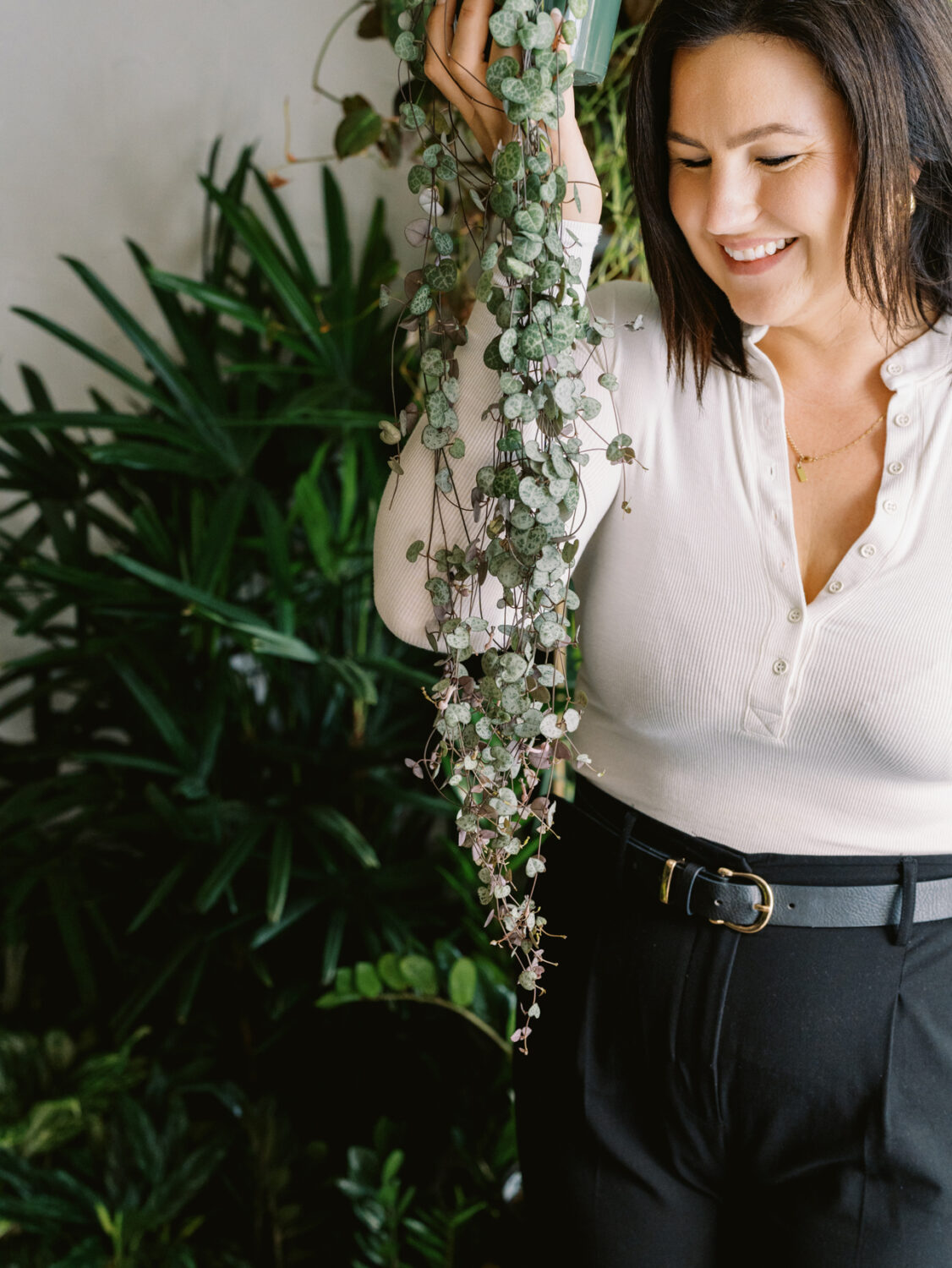 woman in white blouse holding a string of hearts plant