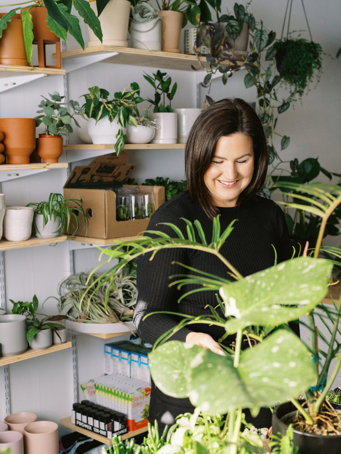 woman with brown hair smiling while surrounded by plants in a store.