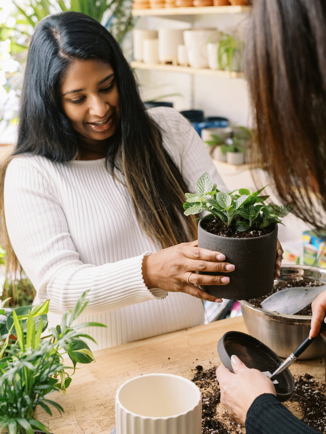 South asian woman in a white dress picking up a potted plant in a store.