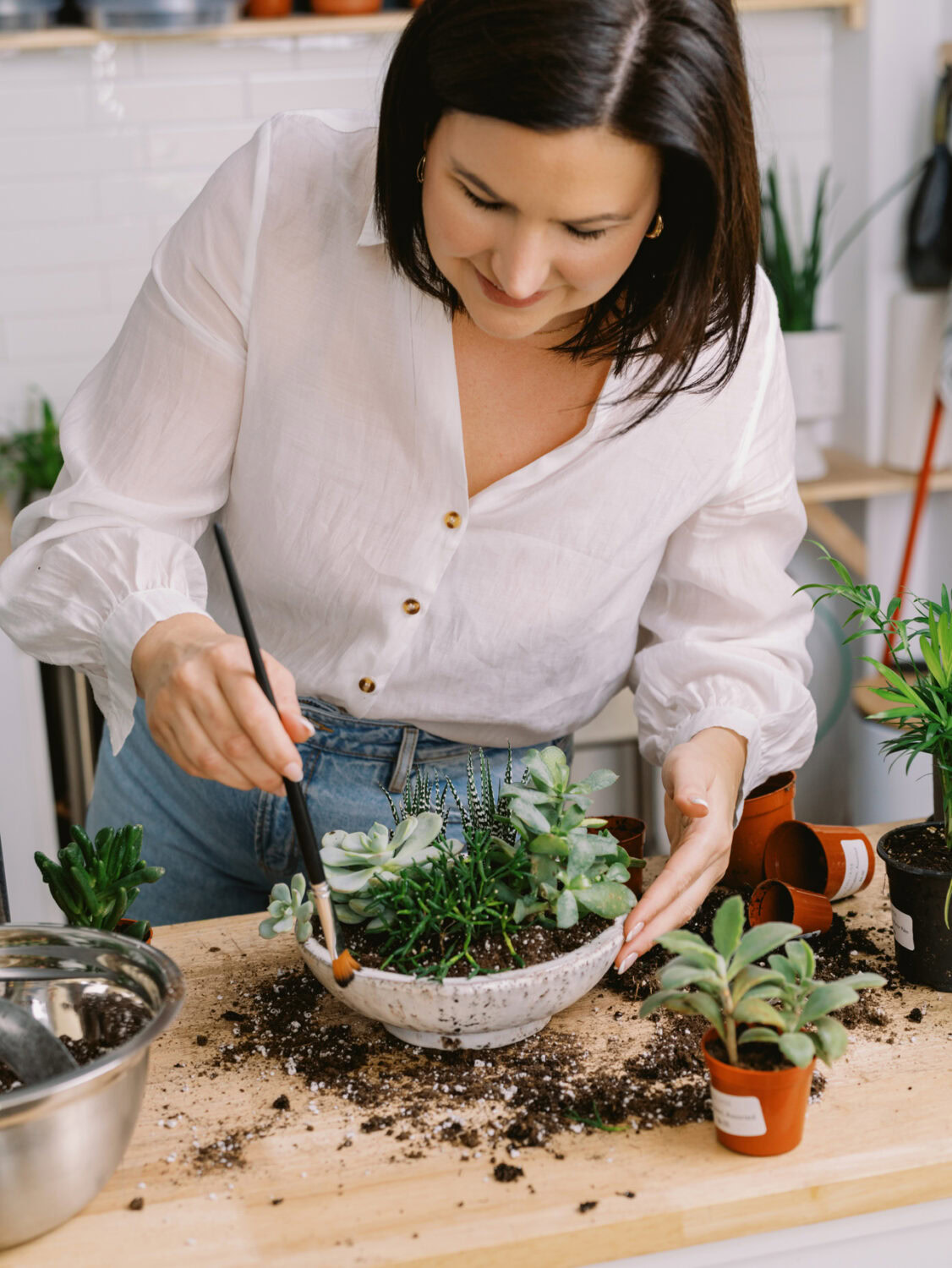 woman using a small brush to clean a pot after putting plants in it.