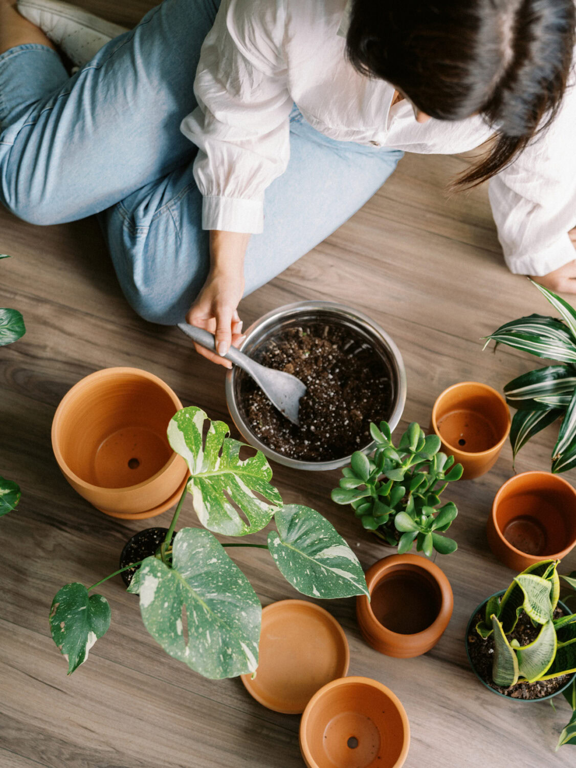 woman sitting on the floor with potting soil, terracotta pots, and plants.