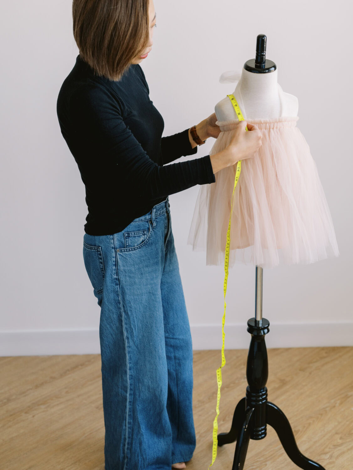 childrens clothing designer measuring a pink tulle dress on a mannequin