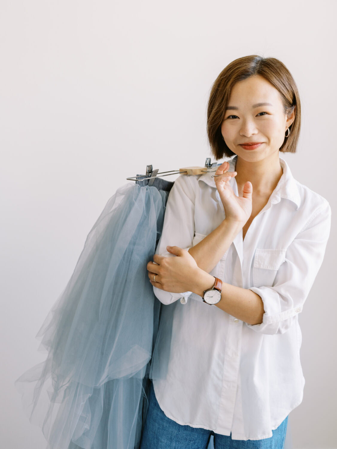 fashion designer in a white shirt holding a garment over her shoulder and smiling at the camera