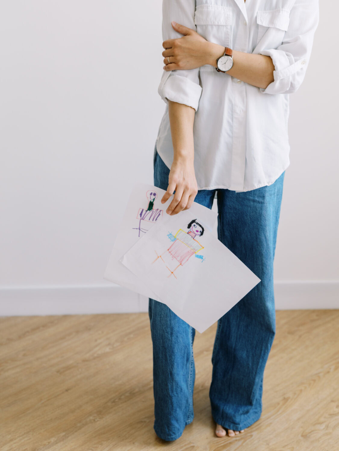 a business woman in white shirt and jeans holding her kids drawings