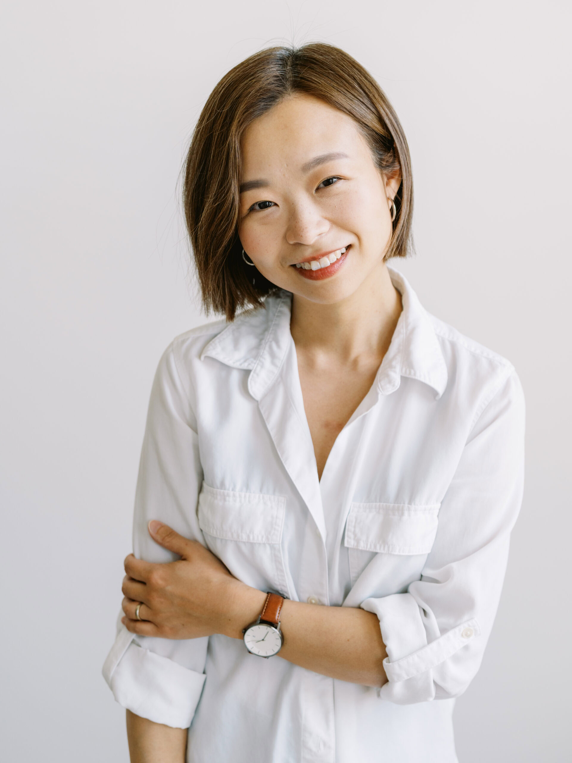 headshot of an asian woman in a white button up tilting her head and smiling at the camera