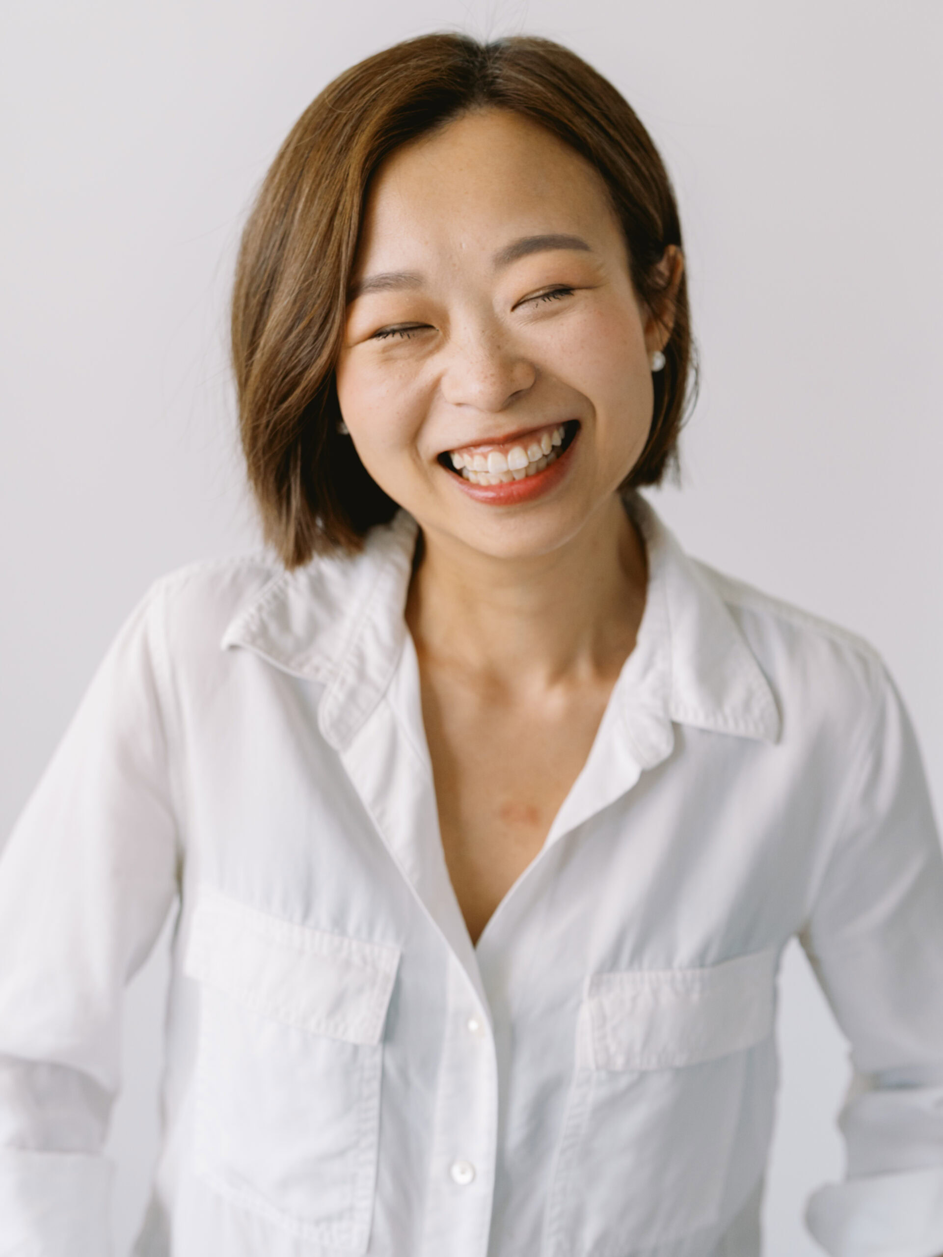 chinese woman in a white button up and bob hair cut laughing with her eyes closed