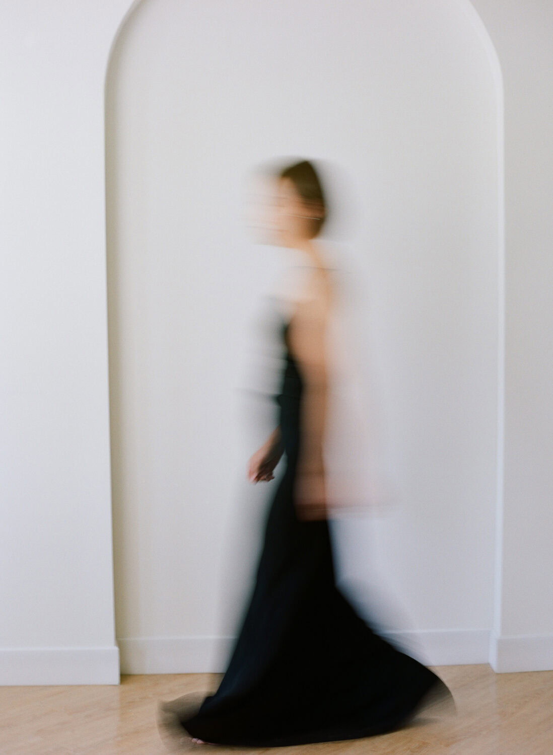 woman with short brown hair and an elegant long black dress blurred by motion walking in front of the camera