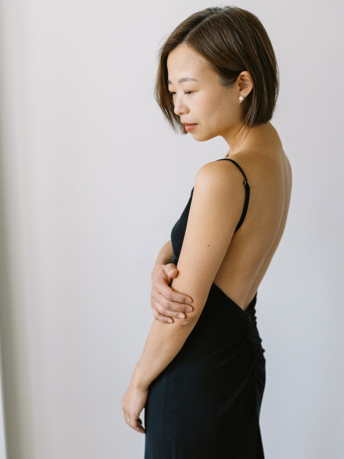 woman with short hair in an elegant backless black dress standing sideways to the camera