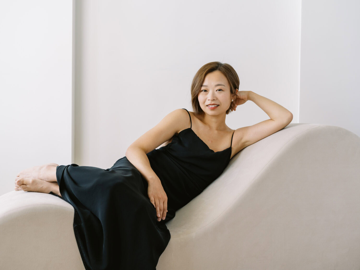 woman in minimalist black dress lounging on a modern chaise looking at the camera
