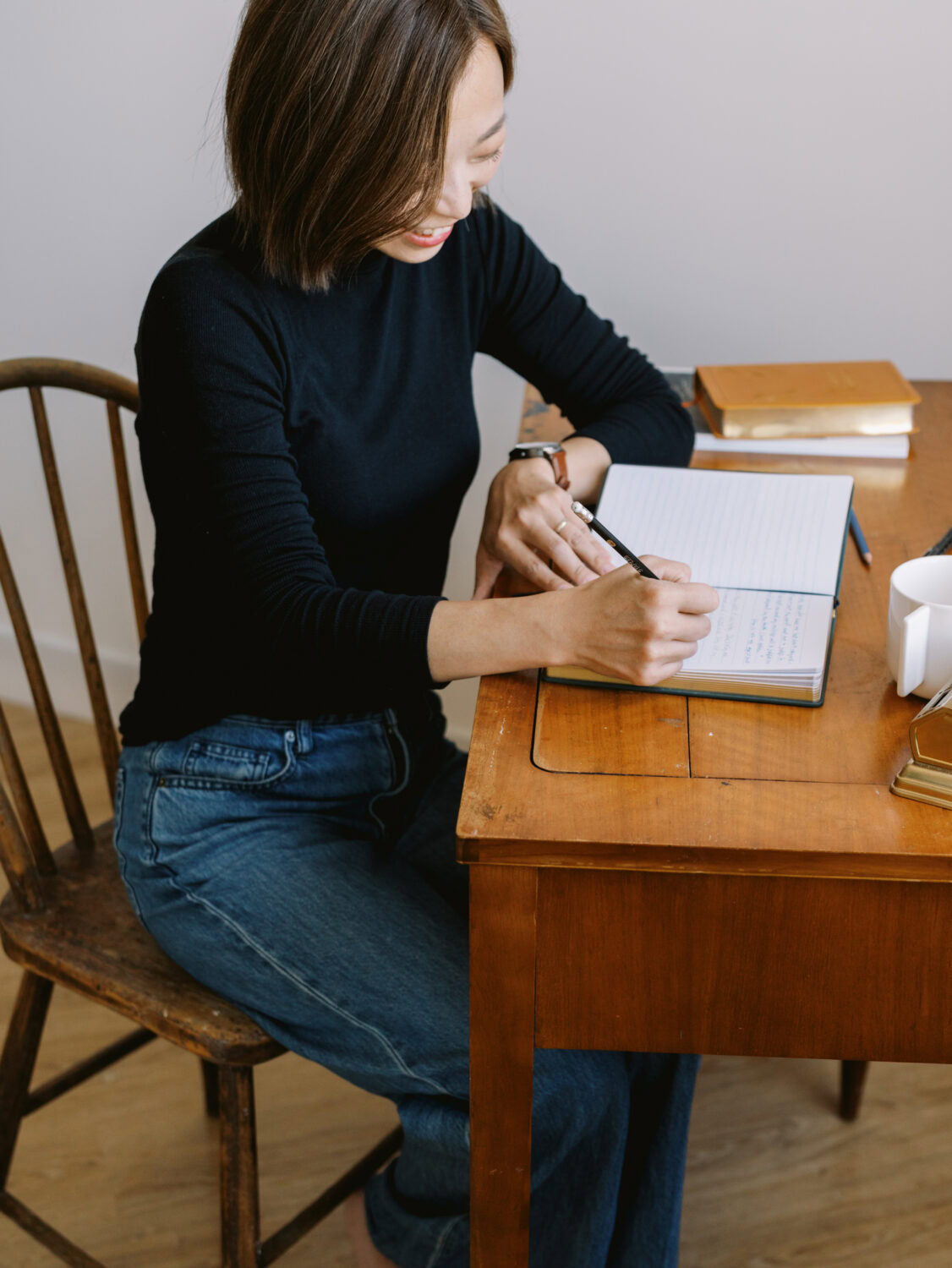 a female author writing in a notebook at a vintage desk in a black shirt and jeans