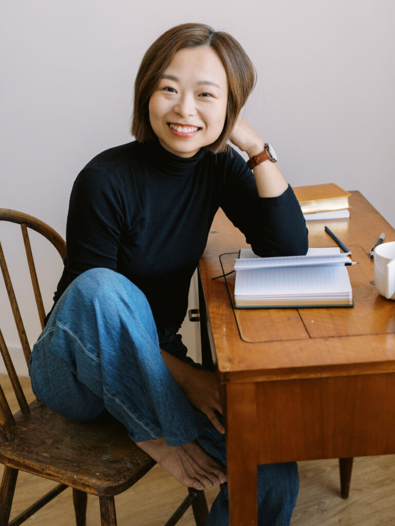 female writer in a black turtleneck and jeans sitting at a vintage wood desk